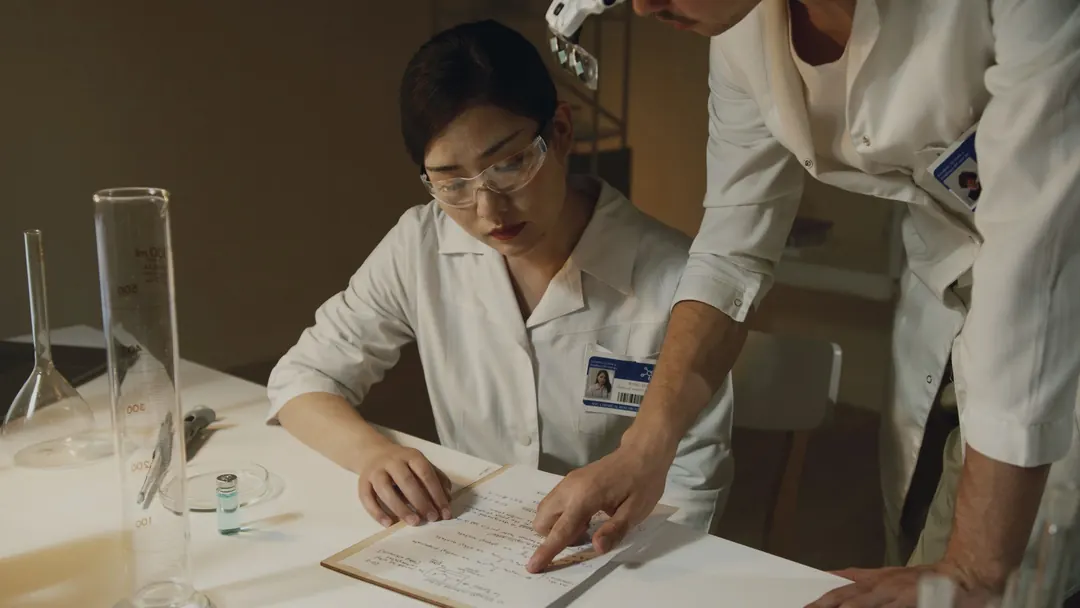 Two scientists review handwritten results together at a lab table.