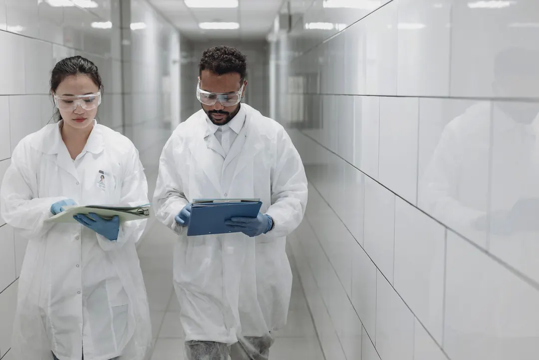 Two researchers read a protocol as they walk a bright laboratory corridor.