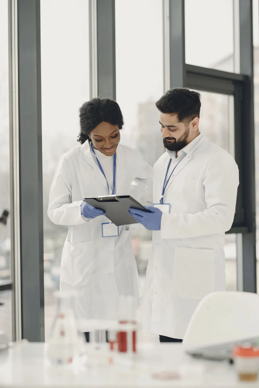 Two scientists compare results on a clipboard by a window.